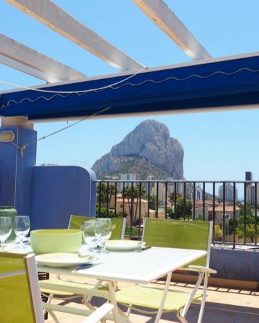 The terrace at Apartamento La Estrella with the table laid under the awning and the Peñón de Ifach behind