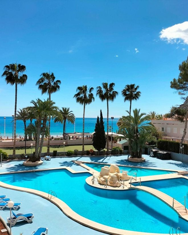 The communal pool at Apartamento Paraíso Mar among palm trees, with the sea behind