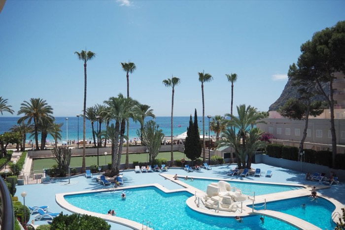 Piscina comunitaria del Apartamento Paraíso Mar rodeada de palmeras, con la playa Levante al fondo