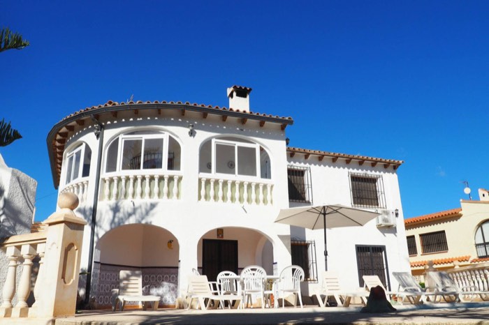 Fachada de Casa Margarita con la terraza acristalada, la sombrilla y la mesa de verano