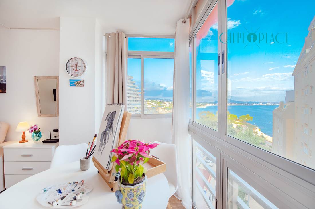 The same room set up as a lounge, with the table, the white chairs and the sea beyond