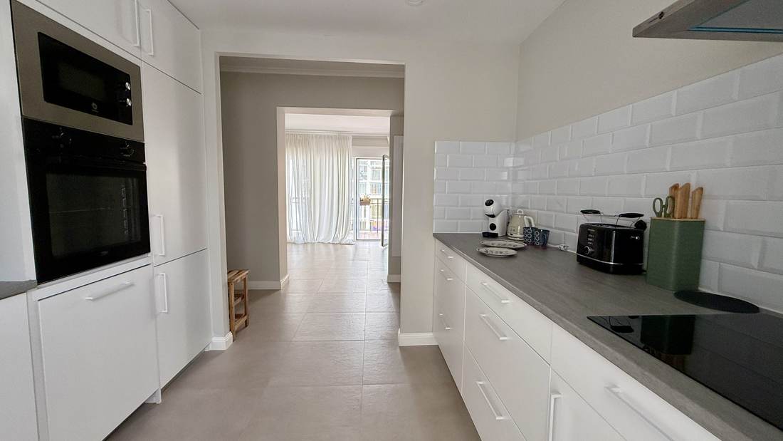 The kitchen along its full length, with the built-in oven and microwave