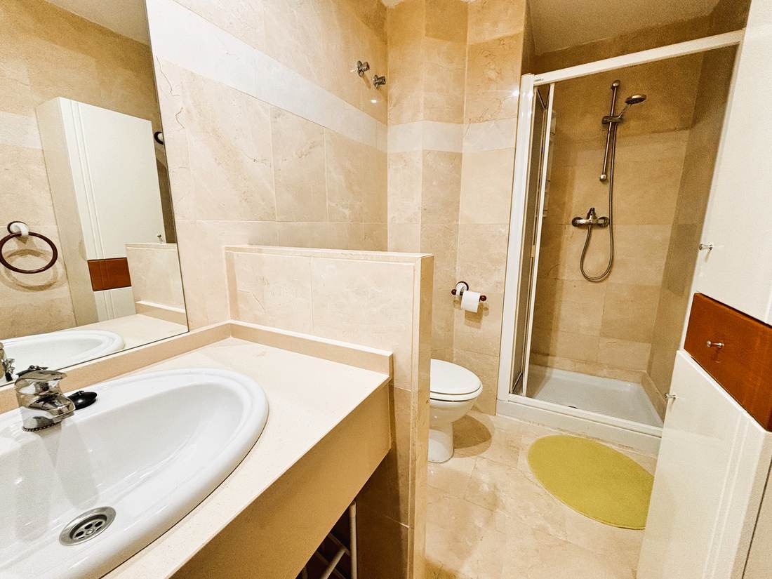 Baño de mármol con lavabo, espejo grande y cabina de ducha