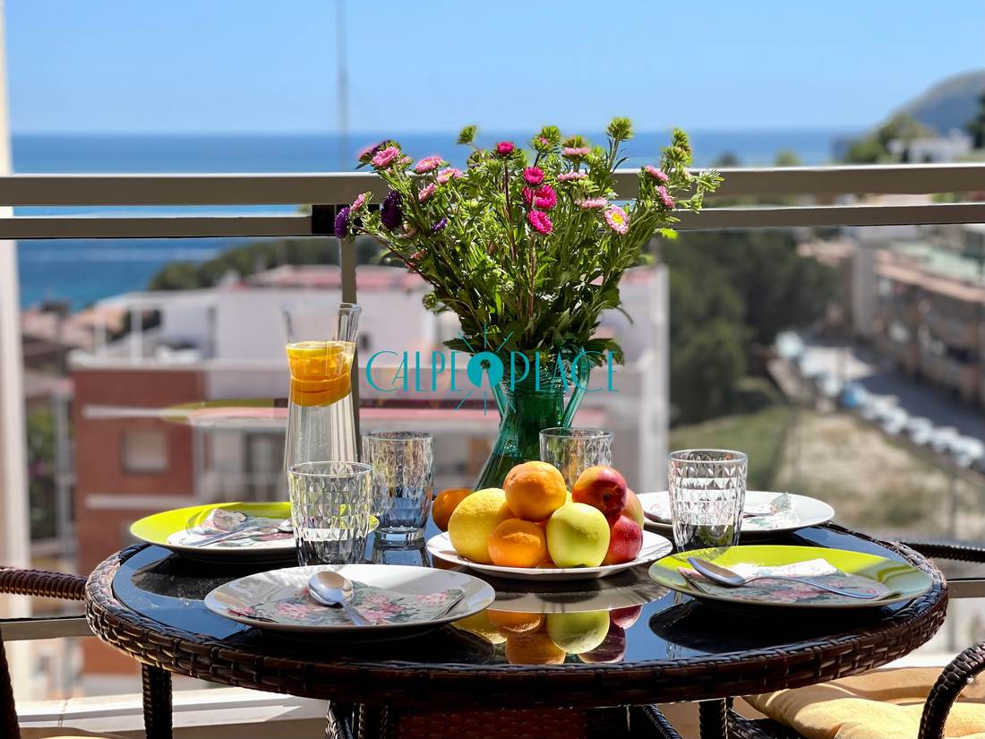 La mesa de la terraza puesta, con flores y el mar detrás