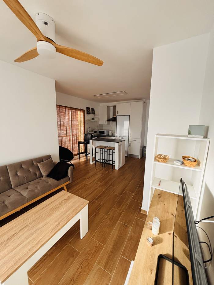 Salón de Porto Bello con sofá de piel, mesa baja de madera y la cocina abierta al fondo