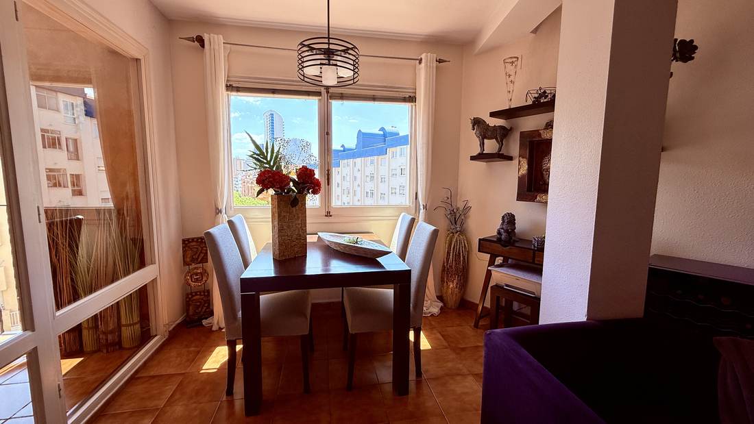 Comedor junto al ventanal, con mesa de cristal y sillas blancas