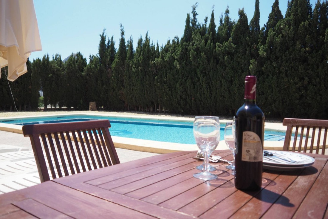 Mesa de madera junto a la piscina, puesta para una cena de verano