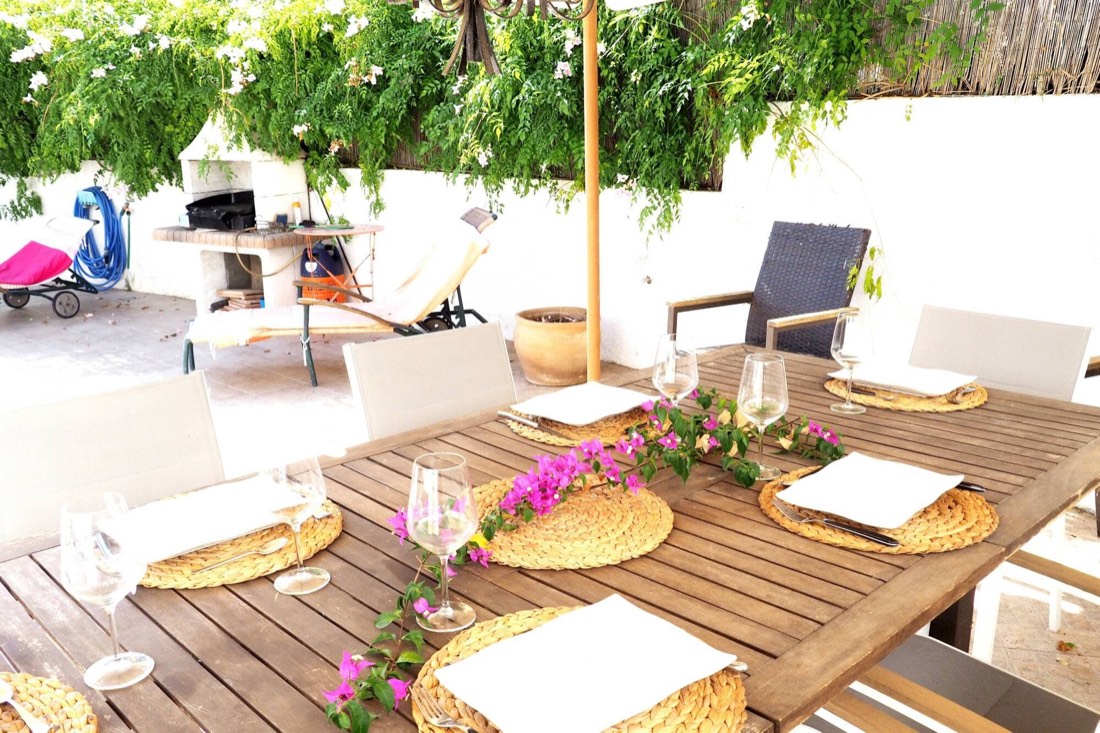 Mesa de exterior puesta bajo la parra, con la barbacoa de obra detrás