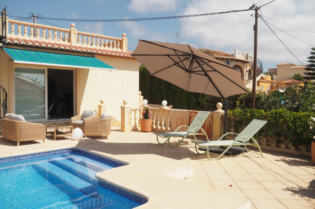 La casa con el toldo verde, la sombrilla y la piscina delante
