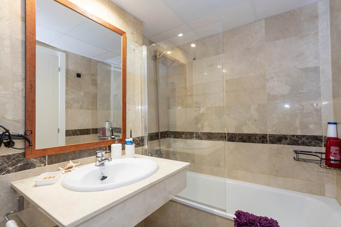Baño completo alicatado en piedra clara, con lavabo, espejo y bañera